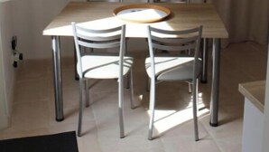 Un coin repas comprenant une table et quatre chaises, une fenêtre à vitrage dépoli et un rideau.