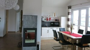 A modern kitchen with white cabinets, a microwave, and a red countertop. There is a dining area with a table and chairs, and a large window providing natural light. - Beach Apartment With sea Views (Glowe)