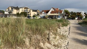 A coastal area with a wooden boardwalk, sandy beach, and houses with red roofs. - Beach Apartment With sea Views (Glowe)