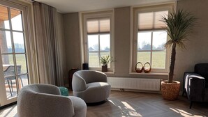 A modern living room with two grey armchairs, a large window with a view, a potted plant, and a radiator. - Villa in Wieringer Near the Wadden Sea (Hippolytushoef)