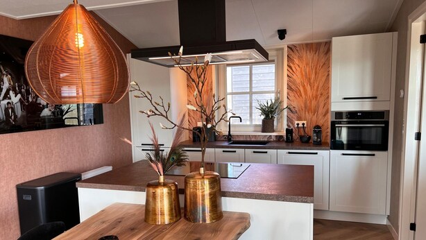 A modern kitchen with white cabinets, a wooden dining table, and a pendant light. - Villa in Wieringer Near the Wadden Sea (Hippolytushoef)