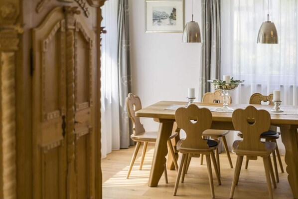 A dining area with a wooden table and chairs, a vase with flowers, and a framed picture on the wall. - Marlena Hollental Chalet (Garmisch-Partenkirchen)