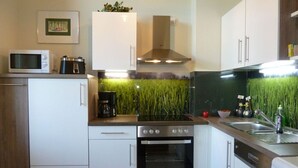 Une cuisine moderne avec des meubles blancs, une cuisinière, un four, un four à micro-ondes et une machine à café.
