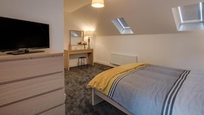 Un dormitorio con cama, escritorio, televisión y tragaluz.