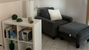 A small, modern living room with a grey sofa, a white bookshelf, and a small table with decorative items. - Holiday Apartment Leah (Toenning)