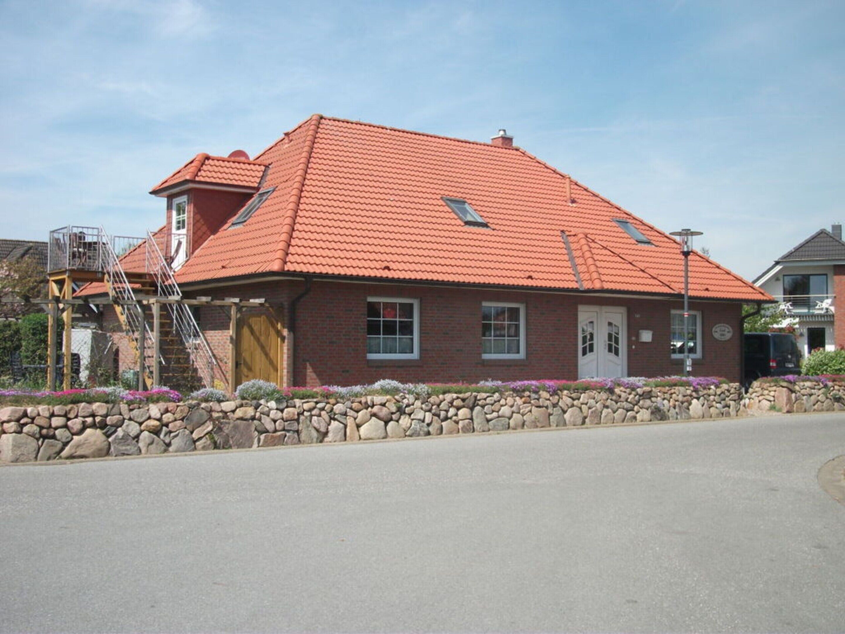 A brick building with a red-tiled roof, a stone wall in front, and a small staircase leading to a balcony.
