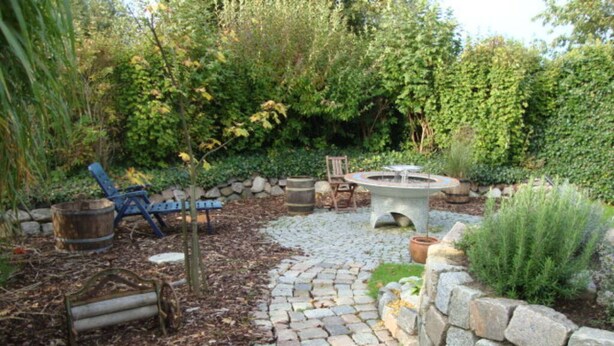 A garden patio with a stone pathway, a rustic fire pit, and outdoor furniture. - Holiday Apartment Leah (Toenning)