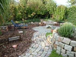 Ein Garten mit einer gepflasterten Terrasse, einer rustikalen Feuerstelle und Gartenmöbeln.