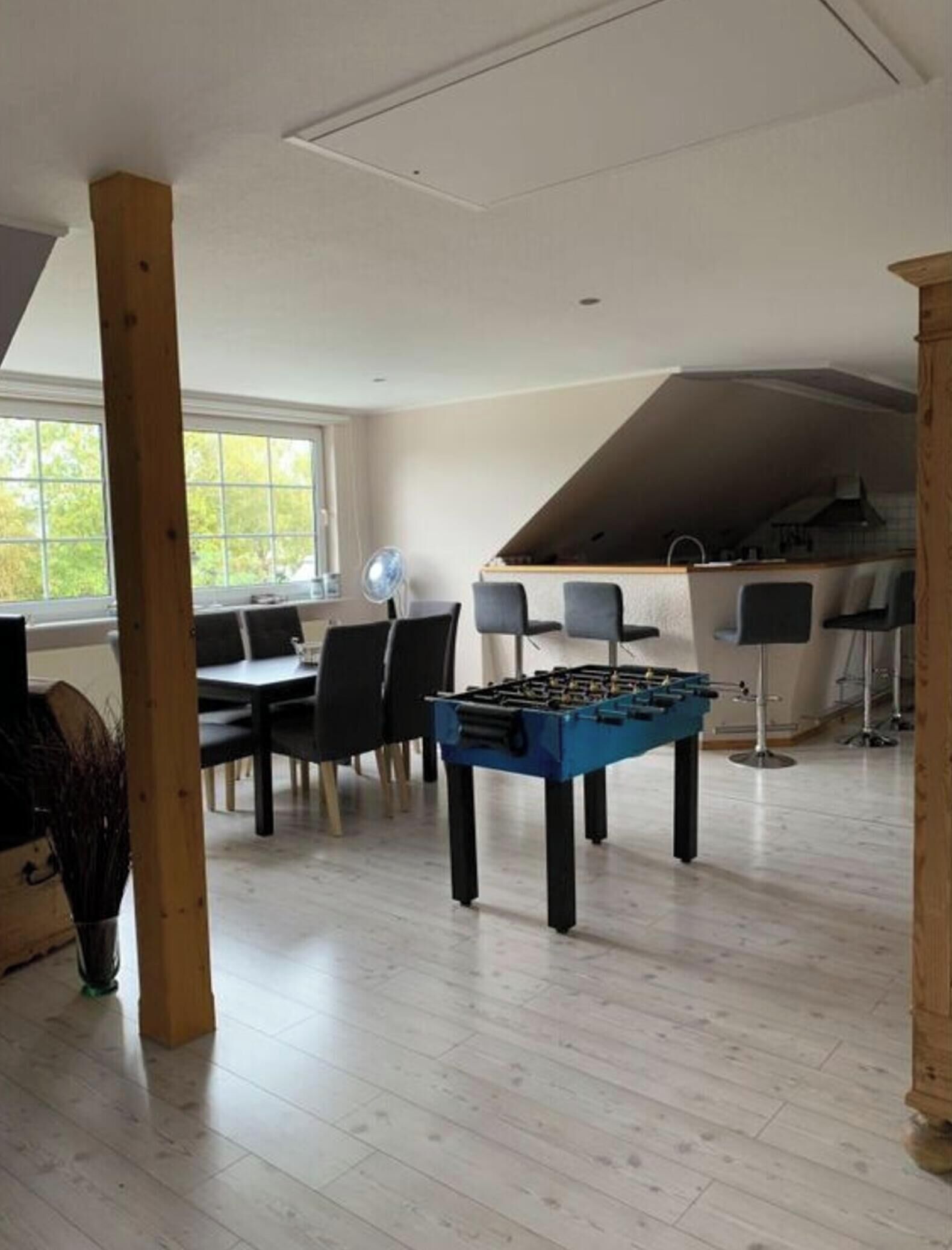 Una habitación amplia con mesa de futbolín, comedor con sillas y área de cocina con taburetes de bar.
