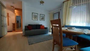 A living room with a sofa, a dining table, and a chair. There are two framed pictures on the wall. - Cosy Holiday Home With Garden (Titisee-Neustadt)