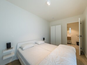 Een slaapkamer met een bed, nachtkastjes, een kledingkast en een zichtbare badkamer door een geopende deur.