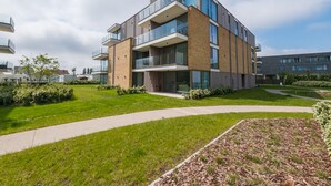 A modern multi-story residential building with balconies, a well-maintained lawn, and a clear sky. - New-build Apartment Near the City Center (Middelkerke)