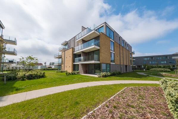Een modern, meerlaags woongebouw met balkons, een verzorgd gazon en een heldere lucht.