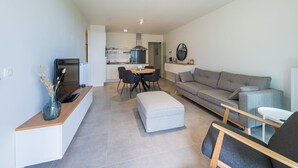 A modern living room with a grey sofa, a dining table with chairs, and a kitchen area in the background. - New-build Apartment Near the City Center (Middelkerke)