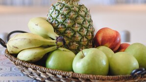 A wicker basket containing a pineapple, bananas, and apples on a patterned tablecloth. - Eugenia studios & apartments  (Rhodes)