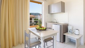 A small kitchenette with a white countertop, a sink, and a coffee maker. There is a table with a fruit basket and a chair. - Eugenia studios & apartments  (Rhodes)