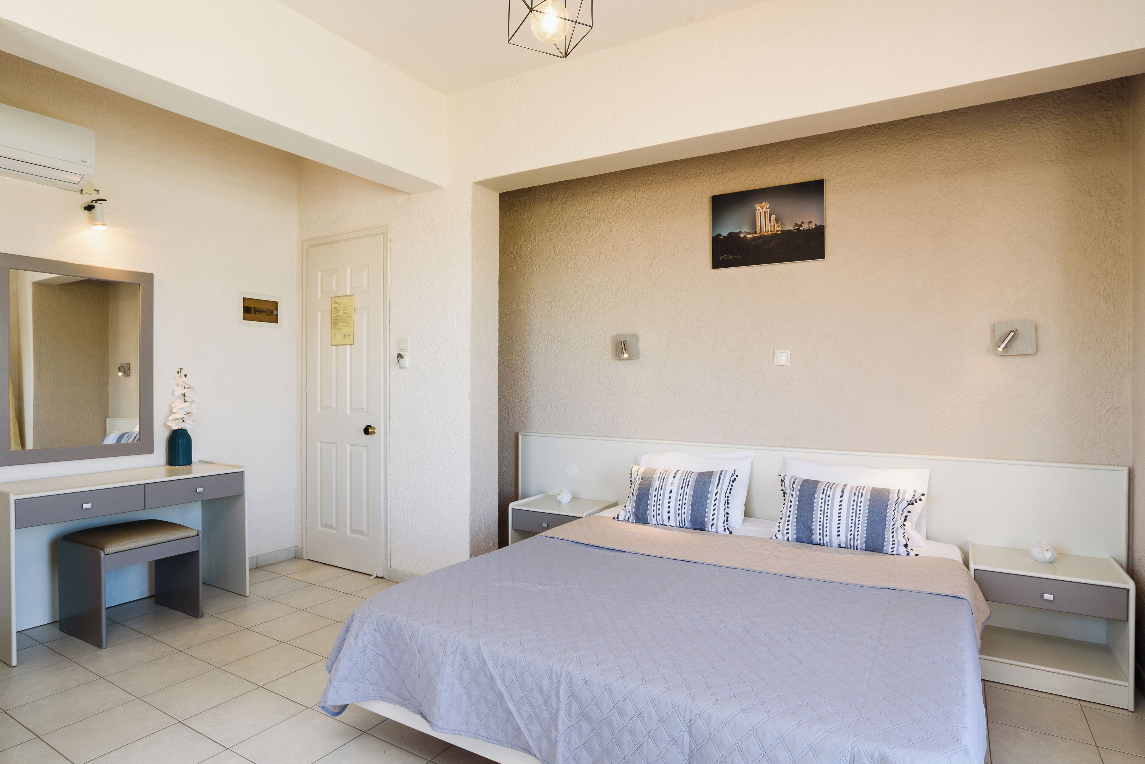 A bedroom with a bed, bedside tables, a desk, a chair, a mirror, and a picture on the wall.