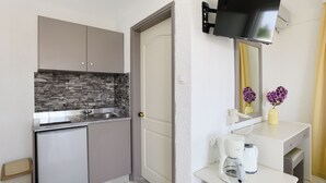 A compact kitchen with a built-in refrigerator, a stone backsplash, and a flat-screen TV mounted above the sink. - Eugenia studios & apartments  (Rhodes)