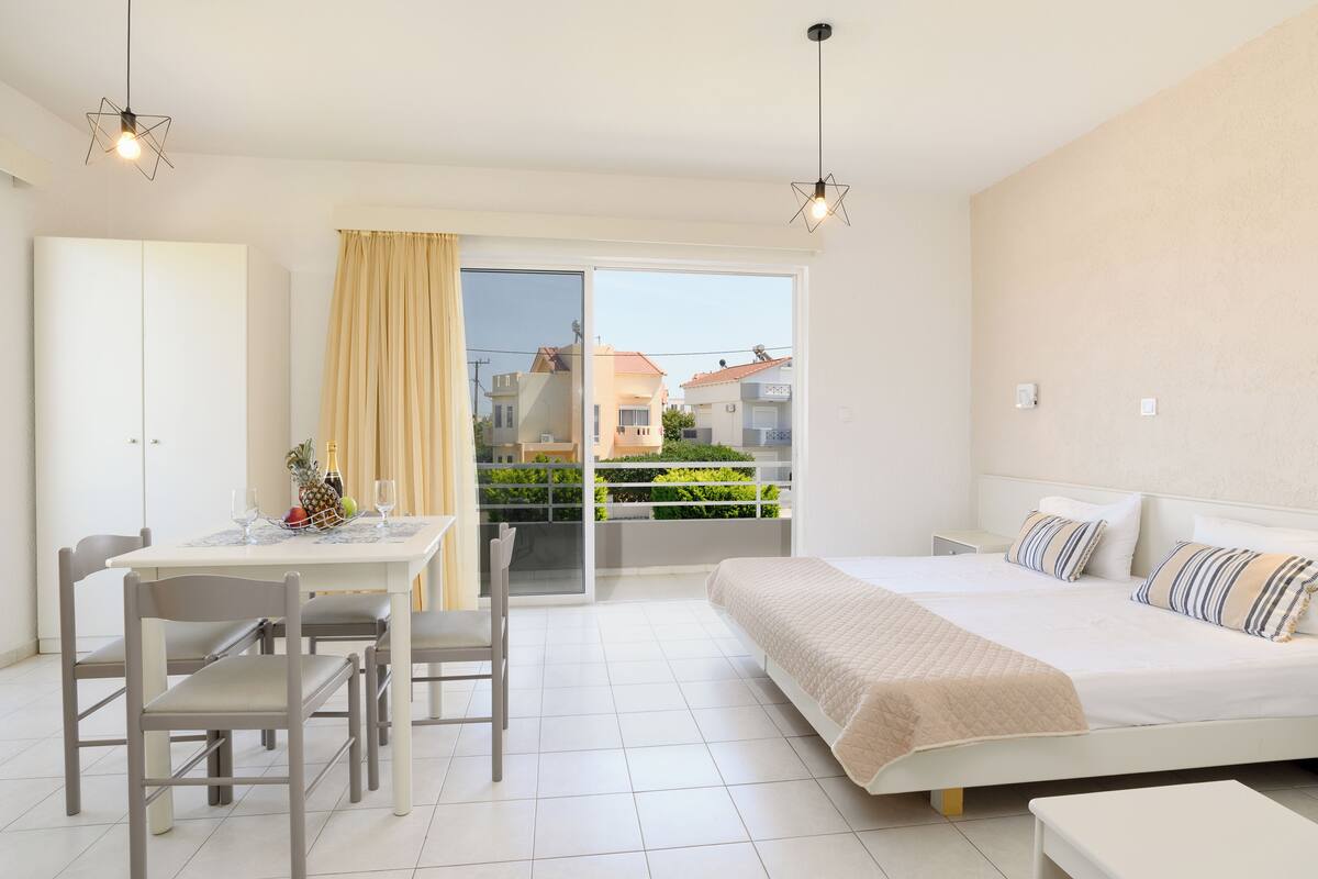 Une chambre moderne avec un grand lit, une table à manger avec des chaises et un balcon offrant une vue sur le quartier.