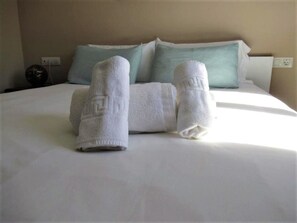 Ein ordentlich bezogenes Bett mit zwei aufgerollten Handtüchern darauf.