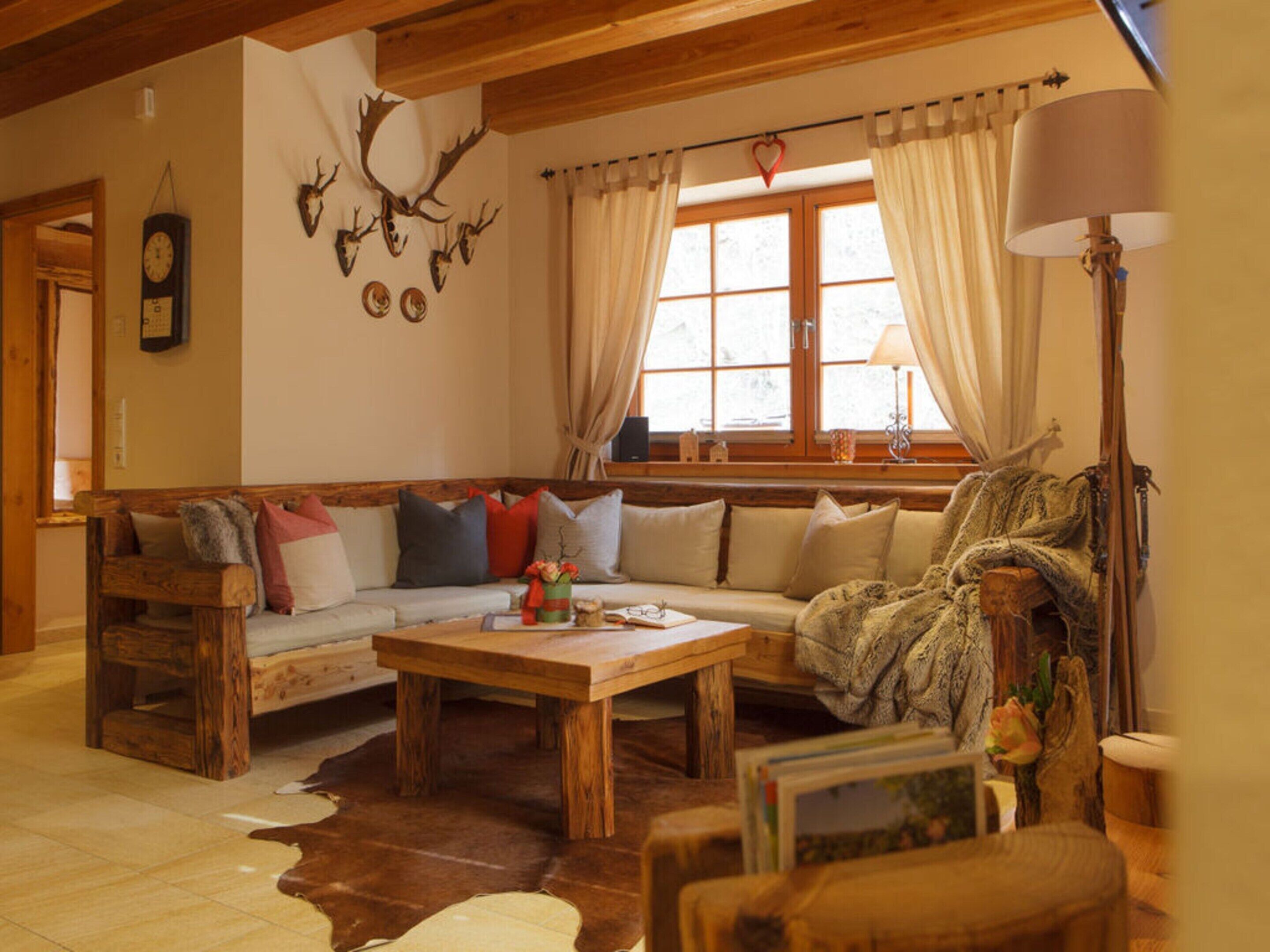A cozy living room with a wooden bench, a sofa, a coffee table, and a large window with curtains.