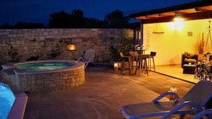 Eine Steinsäule, ein Whirlpool, Liegestühle und ein Tisch mit Stühlen auf einer Terrasse.
