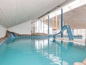 An indoor swimming pool with a blue slide, stone walls, and large windows. - 6 Person Holiday Home on a Holiday Park in Hemmet (Hemmet)