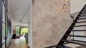 Un intérieur moderne avec un parquet en chevrons, un escalier doté de rampes noires et un mur orné d’un motif géométrique en carreaux.