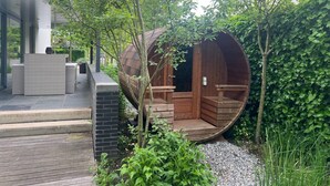 Un espace de détente extérieur moderne, avec des meubles en osier, une structure en bois rappelant un tonneau et un mur en briques.