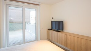 Une chambre d’hôtel avec un lit, un téléviseur posé sur une commode en bois et une porte-fenêtre coulissante donnant sur un balcon.