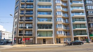Un immeuble résidentiel à plusieurs étages, doté de balcons, d’une entrée au niveau du sol et d’une devanture visible.