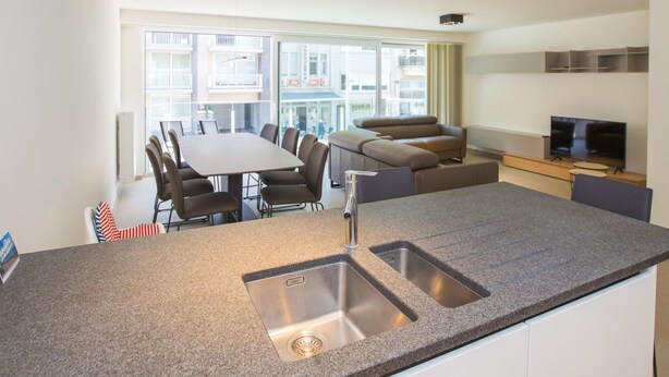 Une cuisine moderne dotée d’un plan de travail en granit, d’un évier en acier inoxydable et d’un coin repas avec une table et des chaises.