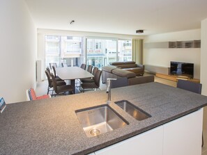 A modern kitchen with a granite countertop, stainless steel sink, and a dining area with a table and chairs. - Apartment in Belgium With Sea View Terrace (Middelkerke)