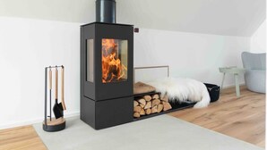 Ein moderner, schwarzer Kaminofen mit Glastür, ein kleiner Holztisch, ein flauschiger weißer Teppich und ein Sessel in einem gemütlichen Raum.