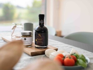 Une bouteille de glaçage balsamique, un bocal d’huile d’olive et un bol de tomates, le tout posé sur une planche en bois.