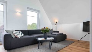 Ein modernes Wohnzimmer mit einem Ecksofa, einem runden Couchtisch und einem flachbildfernseher an der Wand.