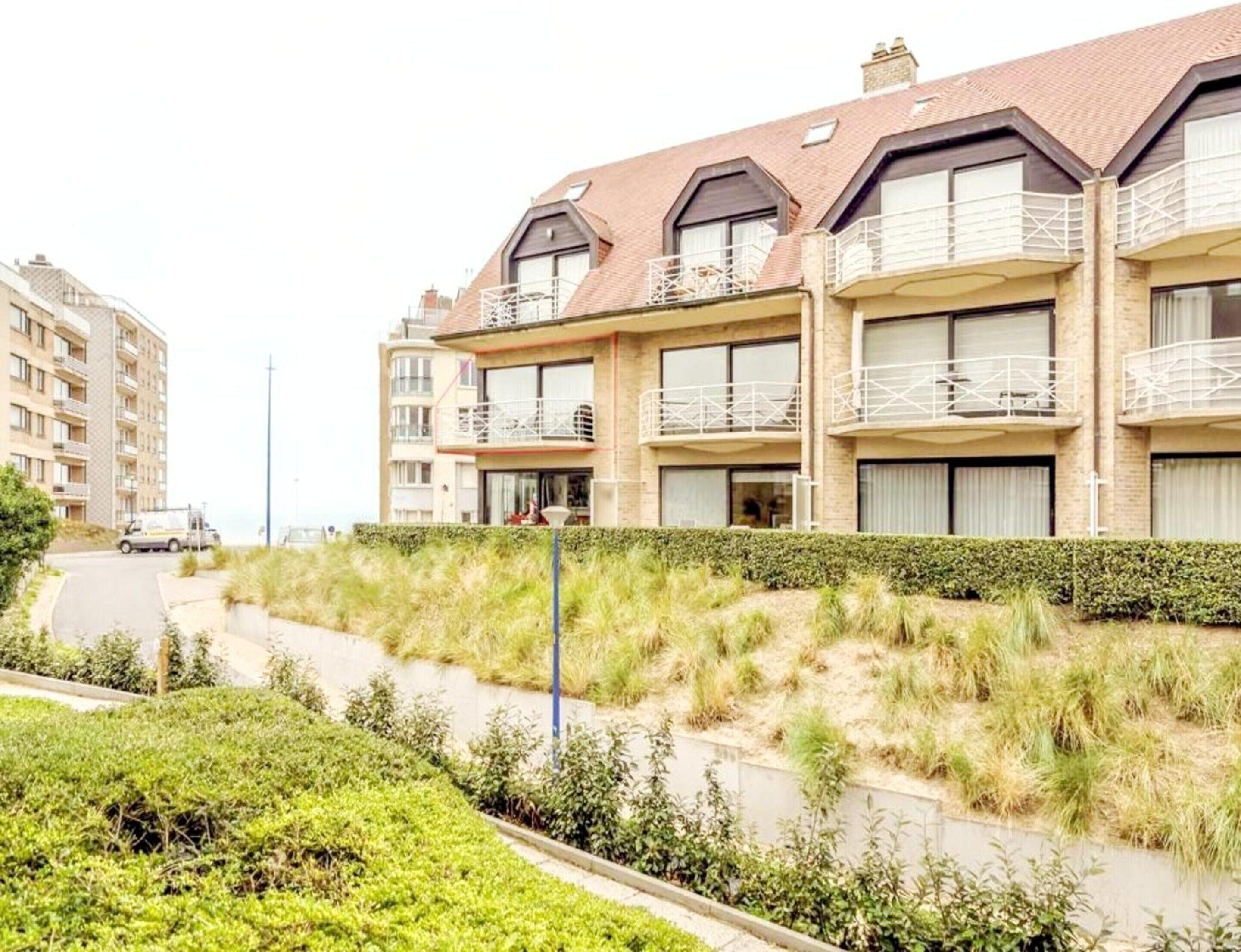 Un edificio residencial de varios pisos con balcones, un sendero empedrado y un área verde.
