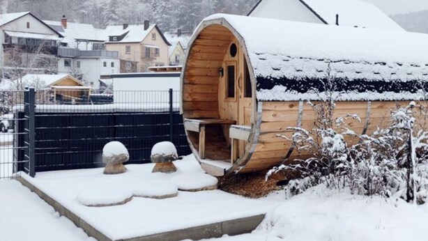 Une cabane en bois, dont le toit est recouvert de neige, et dont l’entrée est circulaire.