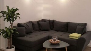 Un salon moderne avec un canapé d’angle gris foncé, une petite table basse ronde et une plante en pot.
