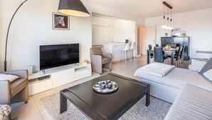 Un salon moderne avec un téléviseur à écran plat, une table basse noire et un canapé. Il y a également un coin cuisine avec une table à manger et des chaises.