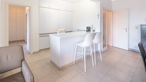 Une cuisine moderne avec des meubles blancs, un îlot central doté de tabourets et une machine à café bien visible.