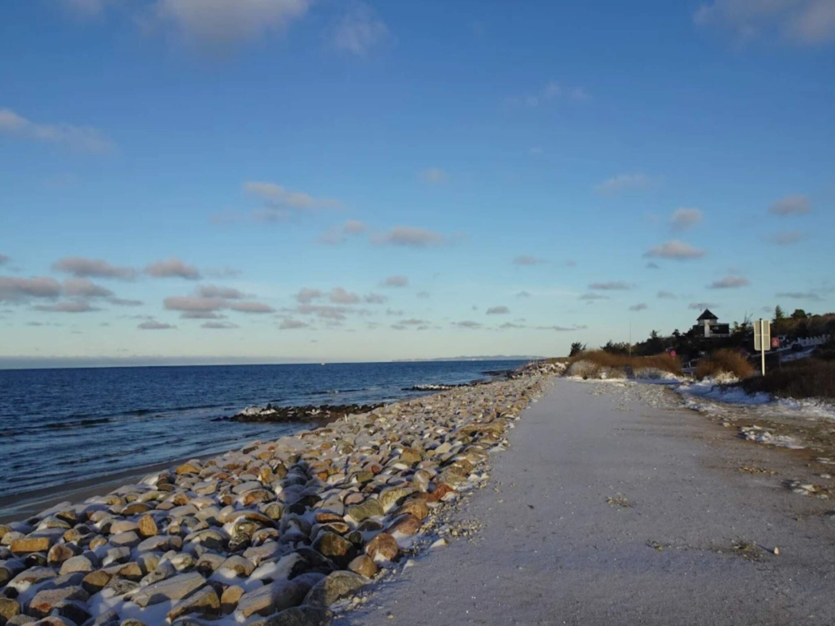 Un sentier rocheux qui longe la plage et mène à la mer, sous un ciel dégagé.