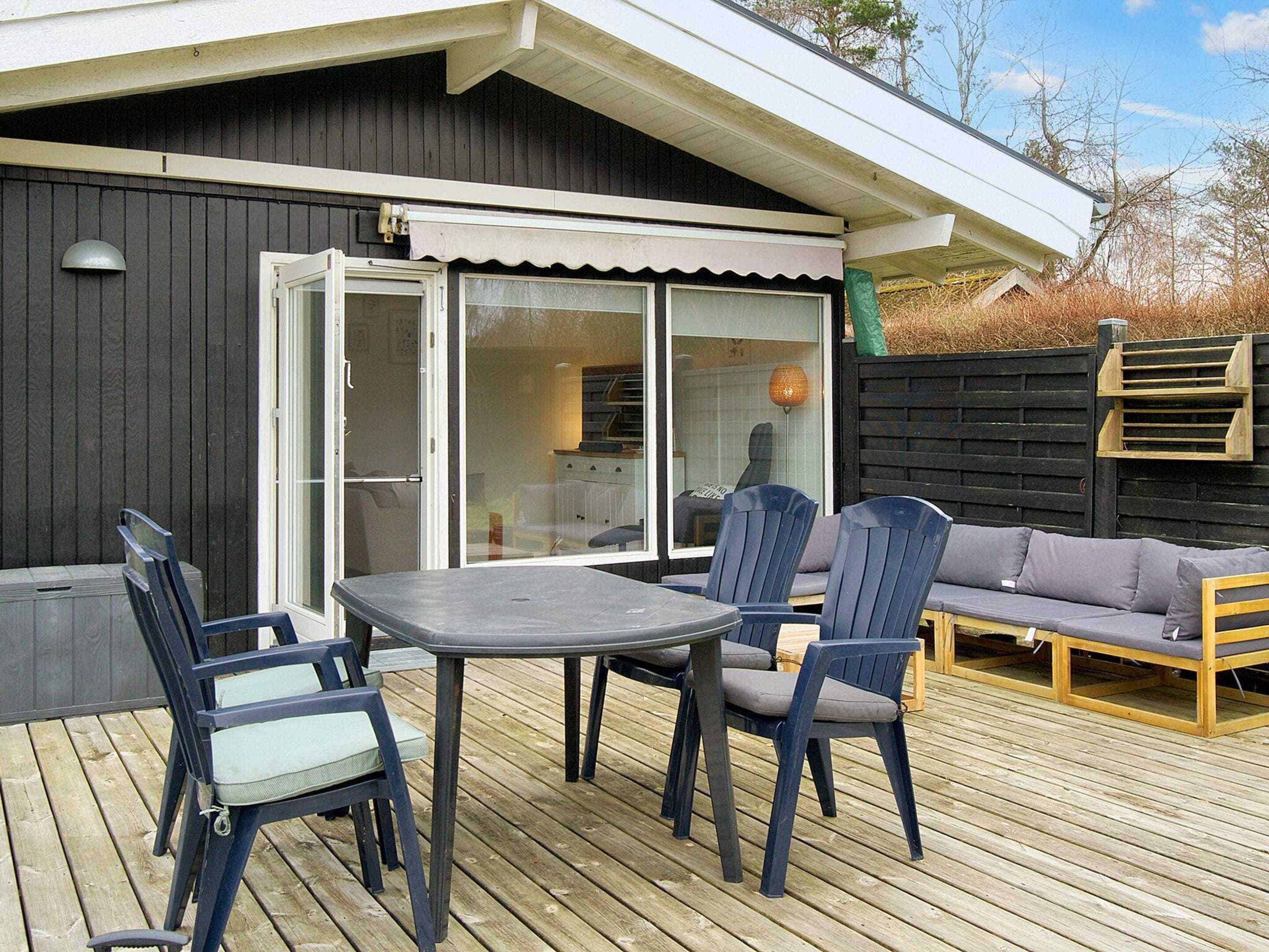 An outdoor deck with a table and chairs, a sofa, and a sliding glass door leading to a kitchen area.
