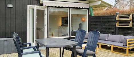 An outdoor deck with a table and chairs, a sofa, and a sliding glass door leading to a kitchen area.