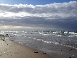 A beach with waves, a pier in the distance, and a cloudy sky.