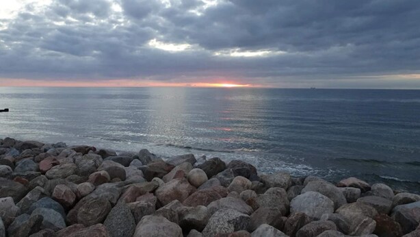 Una costa rocosa con vista al océano y un atardecer en la distancia.
