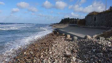 A pebbled beach with a stone wall and a paved walkway leading to a building.