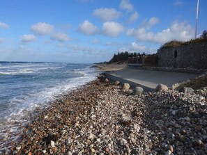 A pebbled beach with a stone wall and a paved walkway leading to a building.