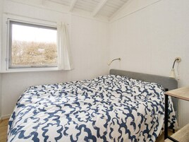 A bedroom with a bed, a window with curtains, a bedside table, and a lamp.