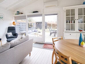 A room with a wooden dining table, a grey sofa, a chair, and a sliding glass door leading to an outdoor patio.